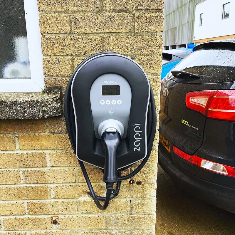 Wall-mounted white EV charge point with digital screen on a brick wall, professional installation in progress