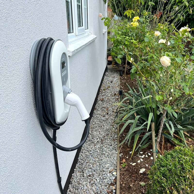 Residential EV charging station mounted on a grey wall next to a window, displaying a clear digital readout, in Hertfordshire