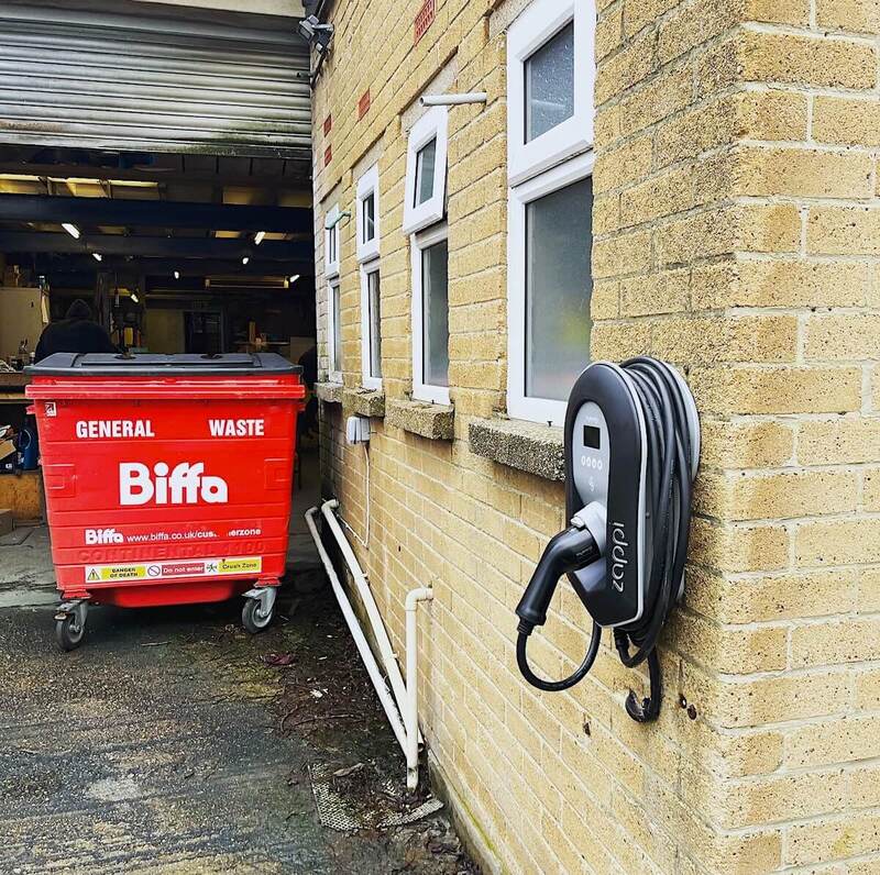 Commercial EV charging station installation with red waste bin in foreground and open workshop in Hertfordshire
