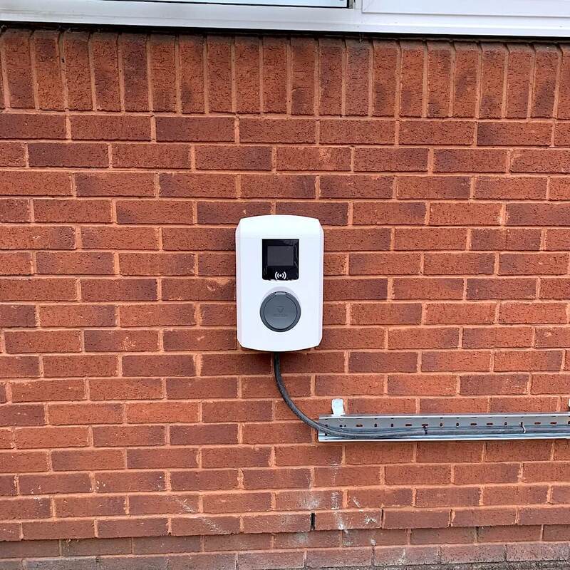 Newly installed EV charging units on red brick wall beside parking lot with safety equipment and installation materials on ground