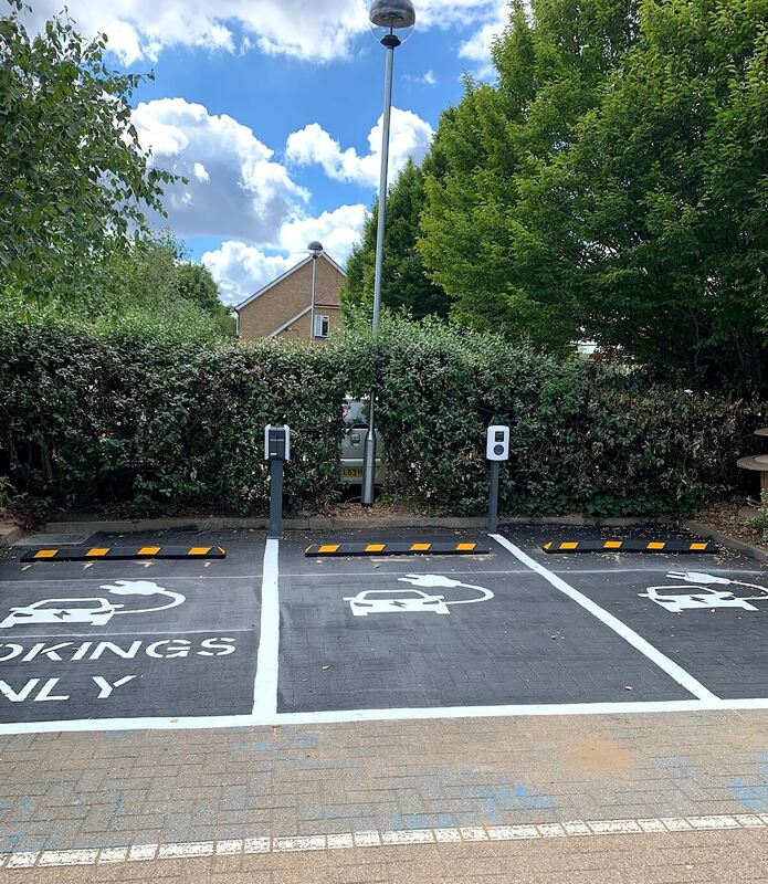 EV charging bays marked for bookings only with electrical charge points in Hertfordshire against lush greenery and clear sky