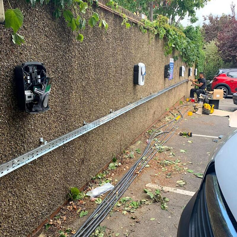 Electricians installing multiple EV charge points along a wall with conduits and wiring in progress